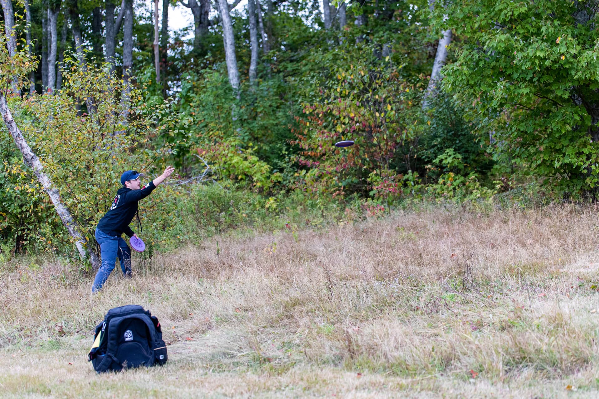 Follow-through as a disc flies across an open fall fairway
